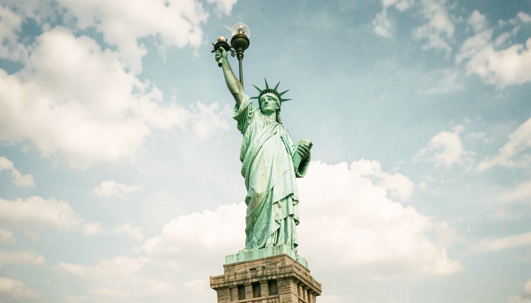 The Statue of Liberty against a bright sky with soft clouds, rendered in muted greens and blues, evoking American travel and freedom