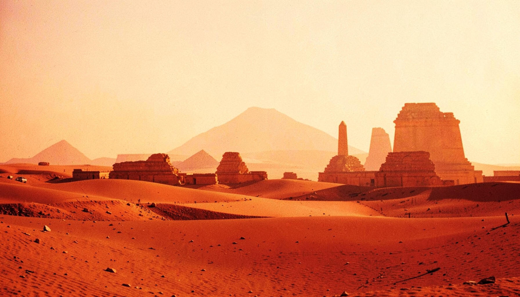 Warm golden desert landscape with the silhouettes of ancient stone monuments under a hazy sky, conveying the timeless atmosphere of Egypt.